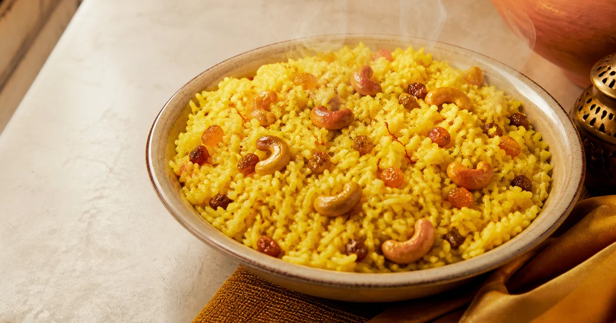 Golden Basanti Polao with separate aromatic rice grains, fried cashews and raisins served in a catering dish.