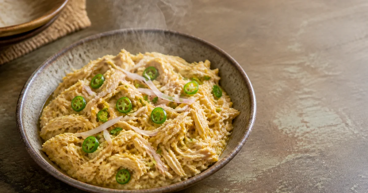 A serving bowl of shredded Bangladeshi chicken bharta finished with mustard oil, fried chillies, onion and fresh coriander.