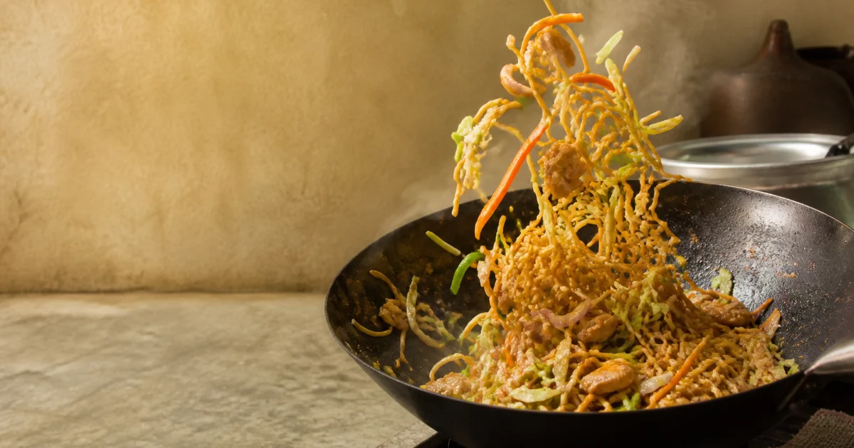 A commercial plate of chicken chowmein with stir-fried noodles, chicken strips, cabbage, carrot, capsicum and spring onion.