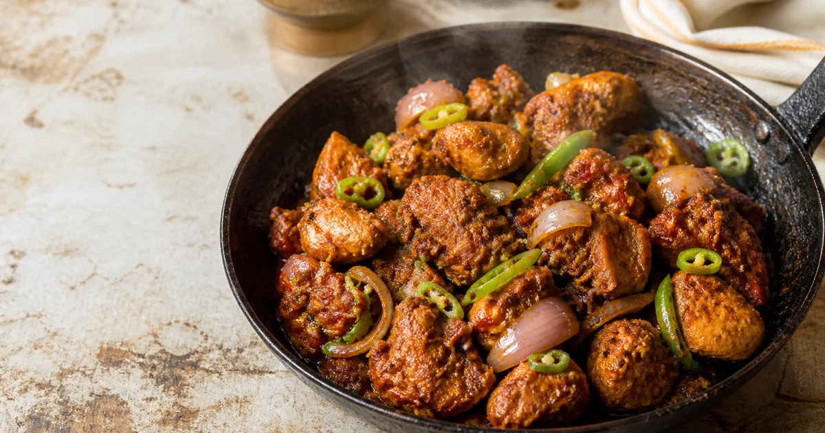 A plate of Bangladeshi chicken jhal fry with bone-in chicken, fried onions, green chillies and thick spicy masala.