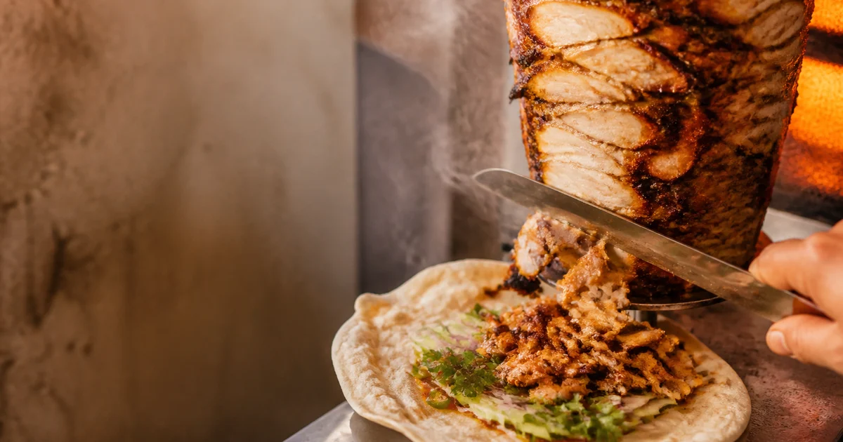 A grilled chicken shawarma wrap filled with thinly shaved chicken, garlic sauce, cabbage, tomato and pickled cucumber.
