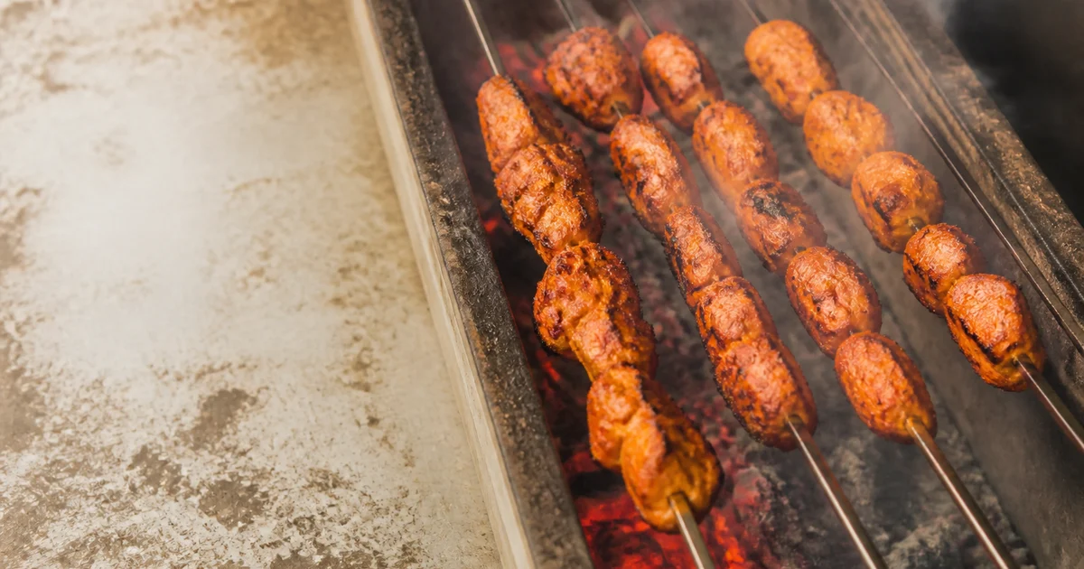 Charred Bangladeshi chicken tikka pieces on metal skewers with sliced onion, lime and green chutney.