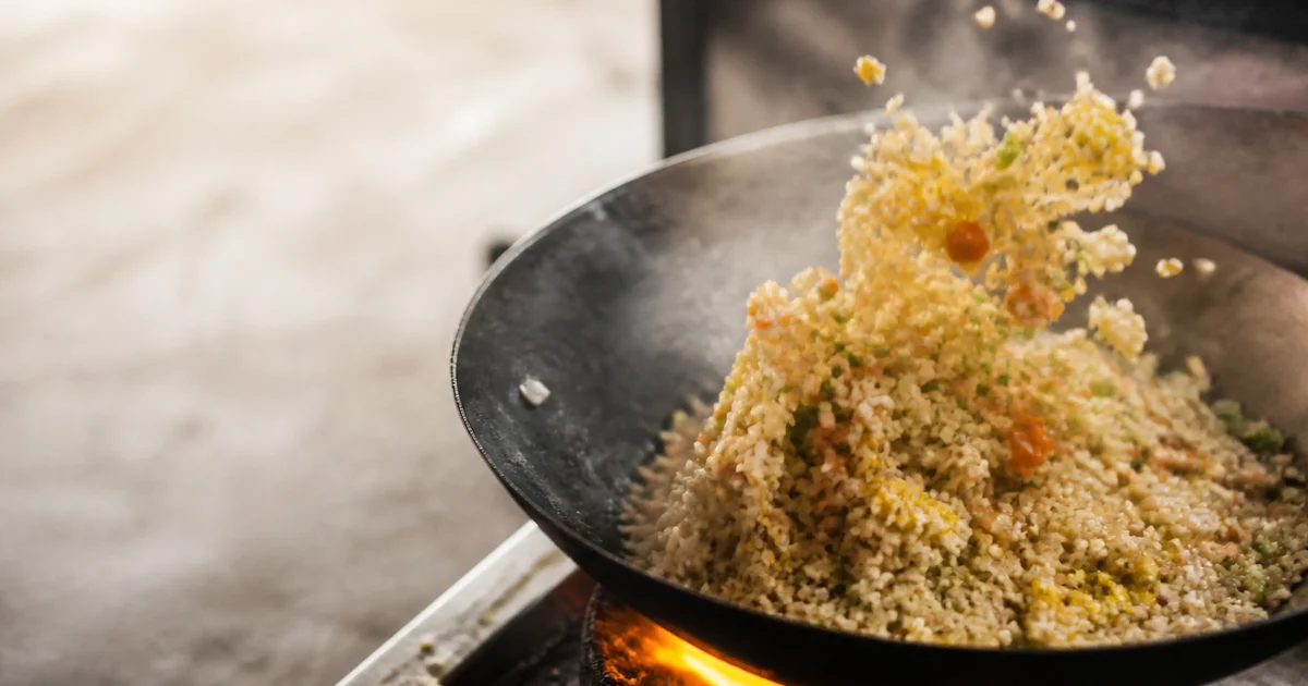 A restaurant portion of Chinese fried rice with chicken, egg, carrots, peas and spring onions served hot from a wok.
