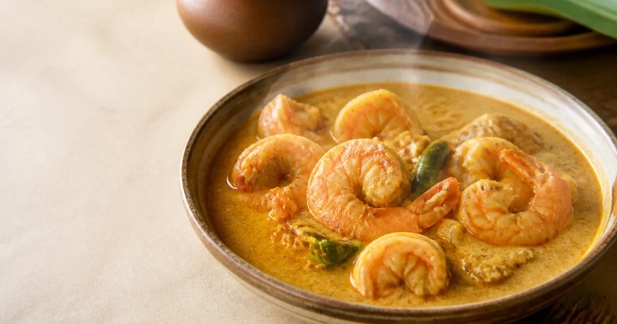Large head-on prawns in a smooth golden coconut milk curry garnished with green chillies.