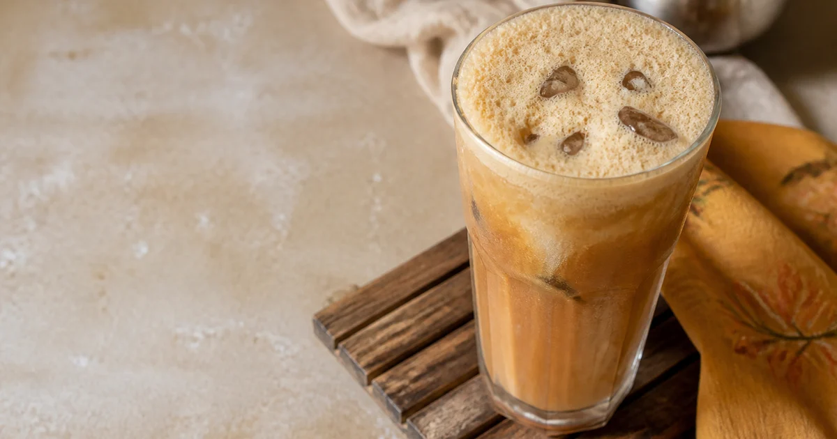A tall glass of frothy cold coffee served chilled with a creamy foam layer and visible condensation.