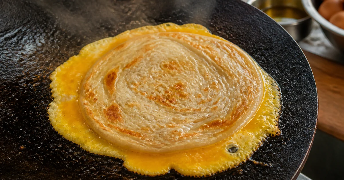 A freshly cooked Bangladeshi egg roll with egg-coated paratha, sliced onion, cucumber, green chilli and sauces wrapped for serving.