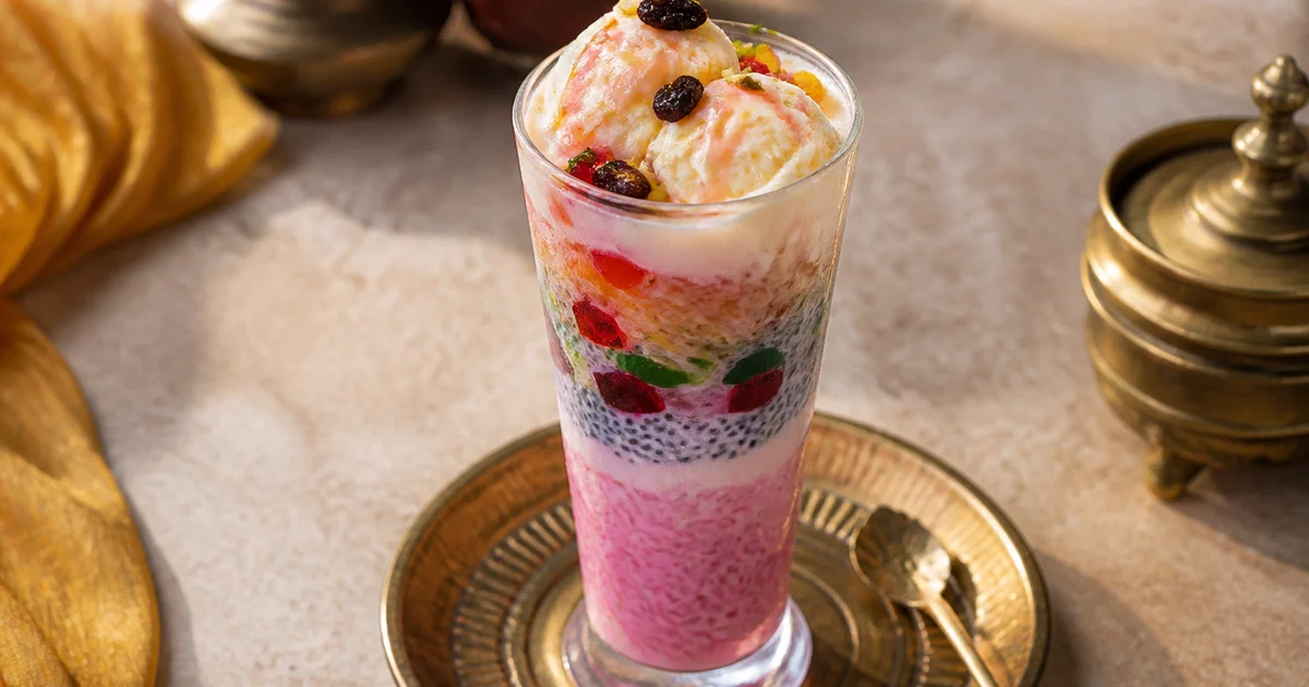A tall glass of Bangladeshi faluda layered with rose milk, jelly, tokma seeds, semai, fruit and a scoop of vanilla ice cream.