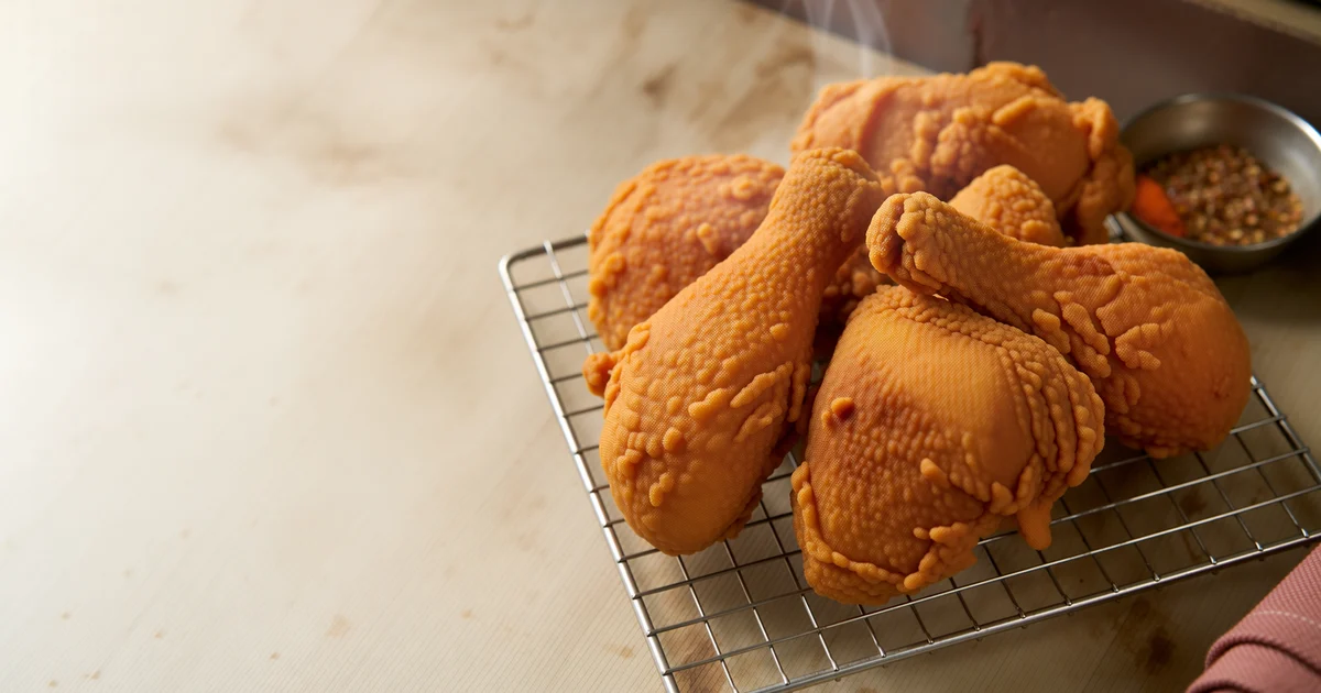 A tray of golden crispy bone-in fried chicken pieces draining on a wire rack after frying.