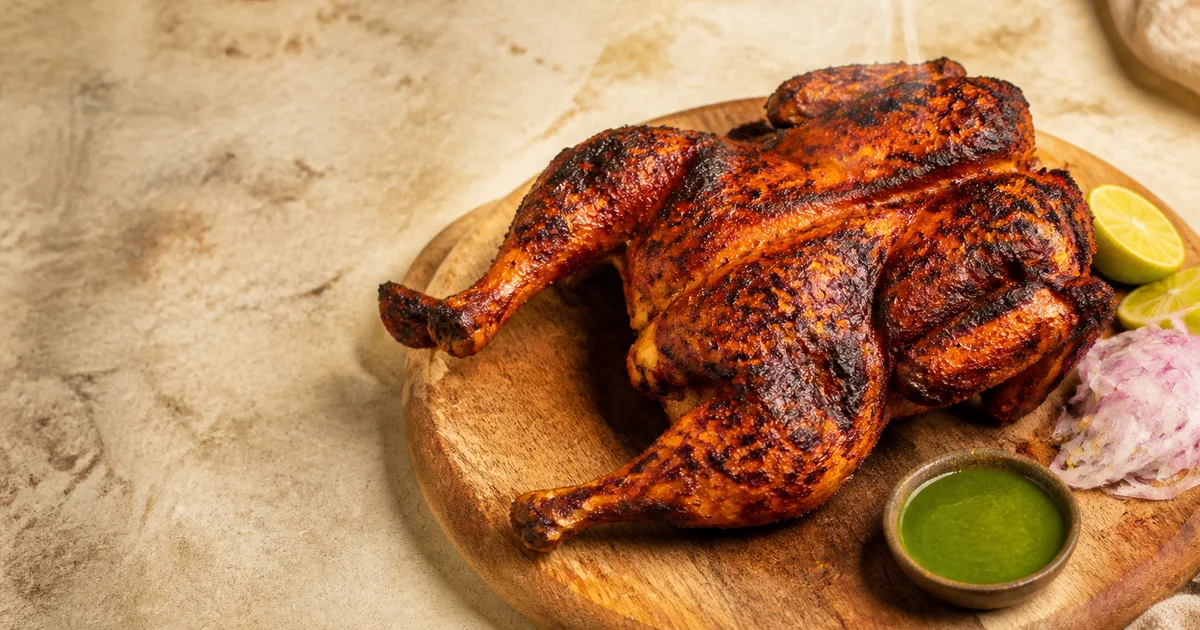 Whole spice-marinated grilled chickens with browned skin turning on a commercial rotisserie.