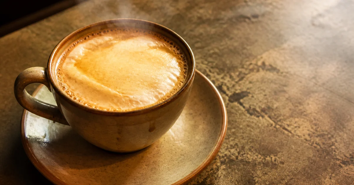 A glass cup of rich Bangladeshi milk tea topped with a thick folded layer of golden malai.