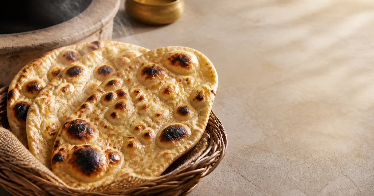 মাটির তন্দুরের পাশে রাখা বাদামি ফোসকা ও হালকা ঘির প্রলেপ দেওয়া টাটকা রেস্টুরেন্ট নান।