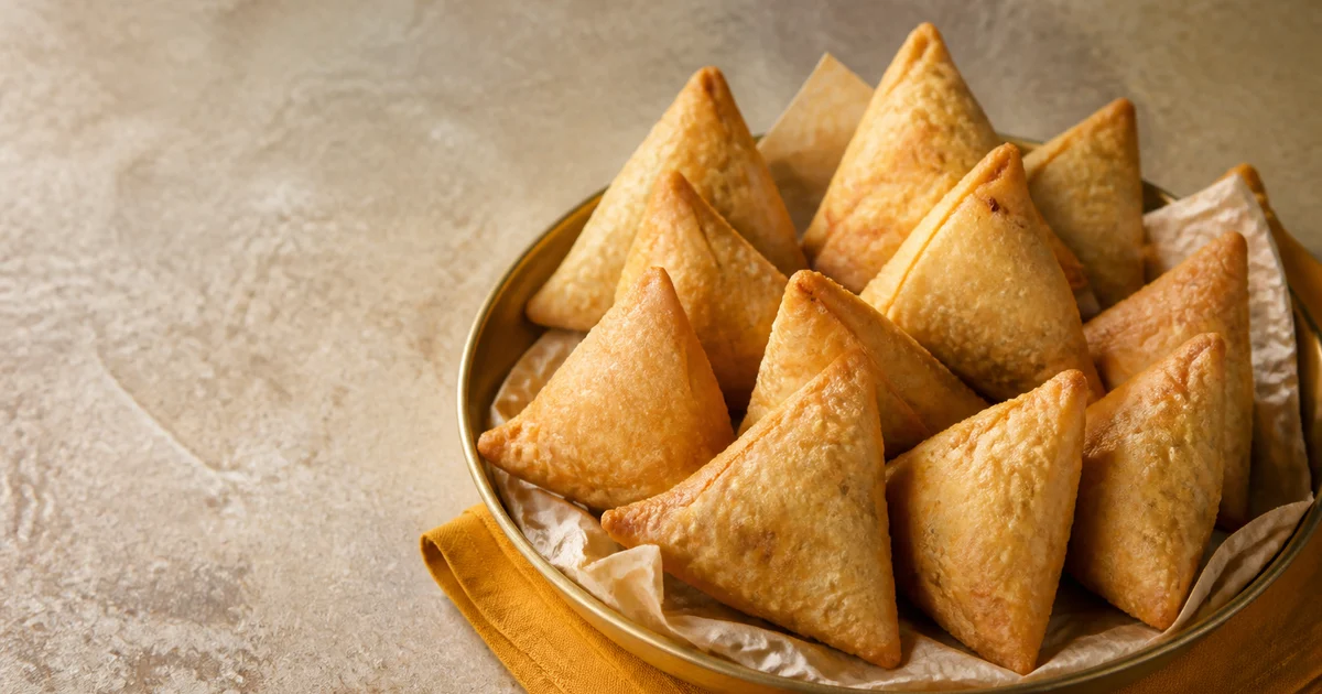 Golden triangular beef samosas draining on a rack with crisp bubbled pastry and sealed edges.