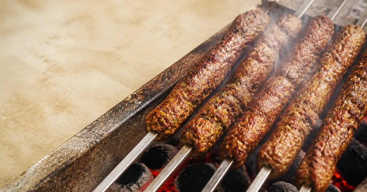 Grilled Bangladeshi beef seekh kebabs with browned ridges and light char arranged beside onion, lemon and green chutney.