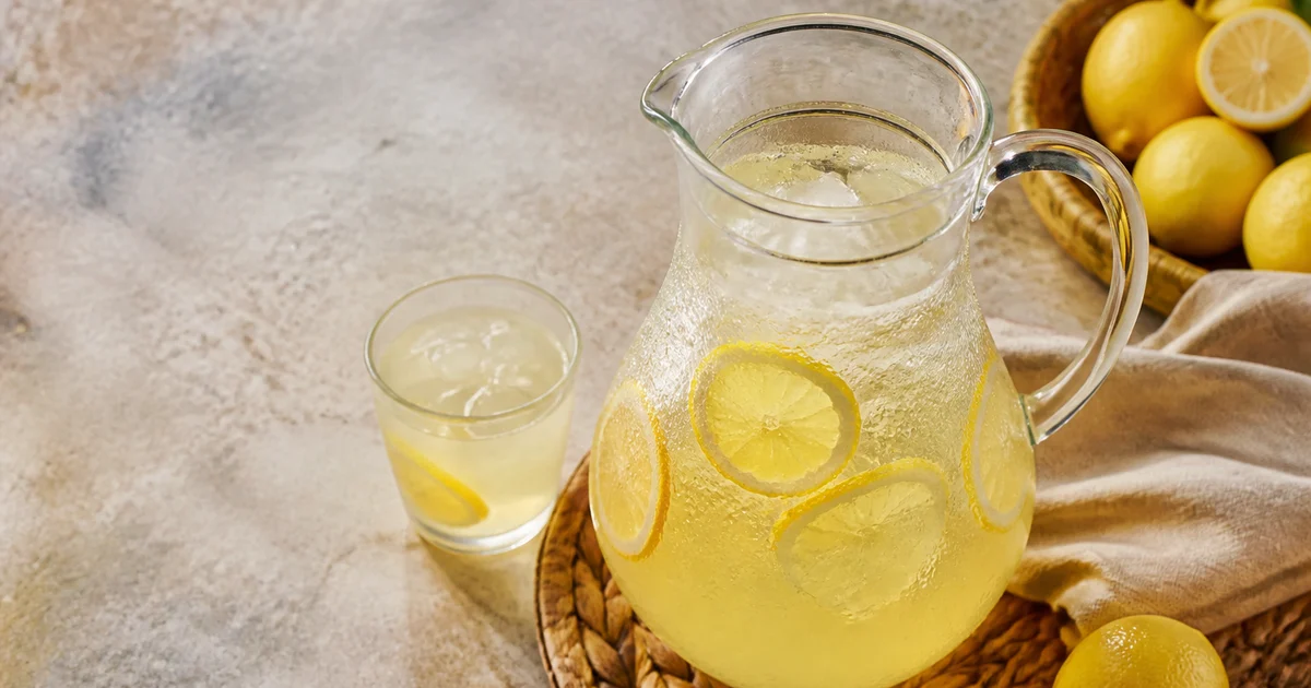 A chilled glass of Bangladeshi lemon sharbat with ice, fresh mint and a lemon slice beside a commercial serving jug.